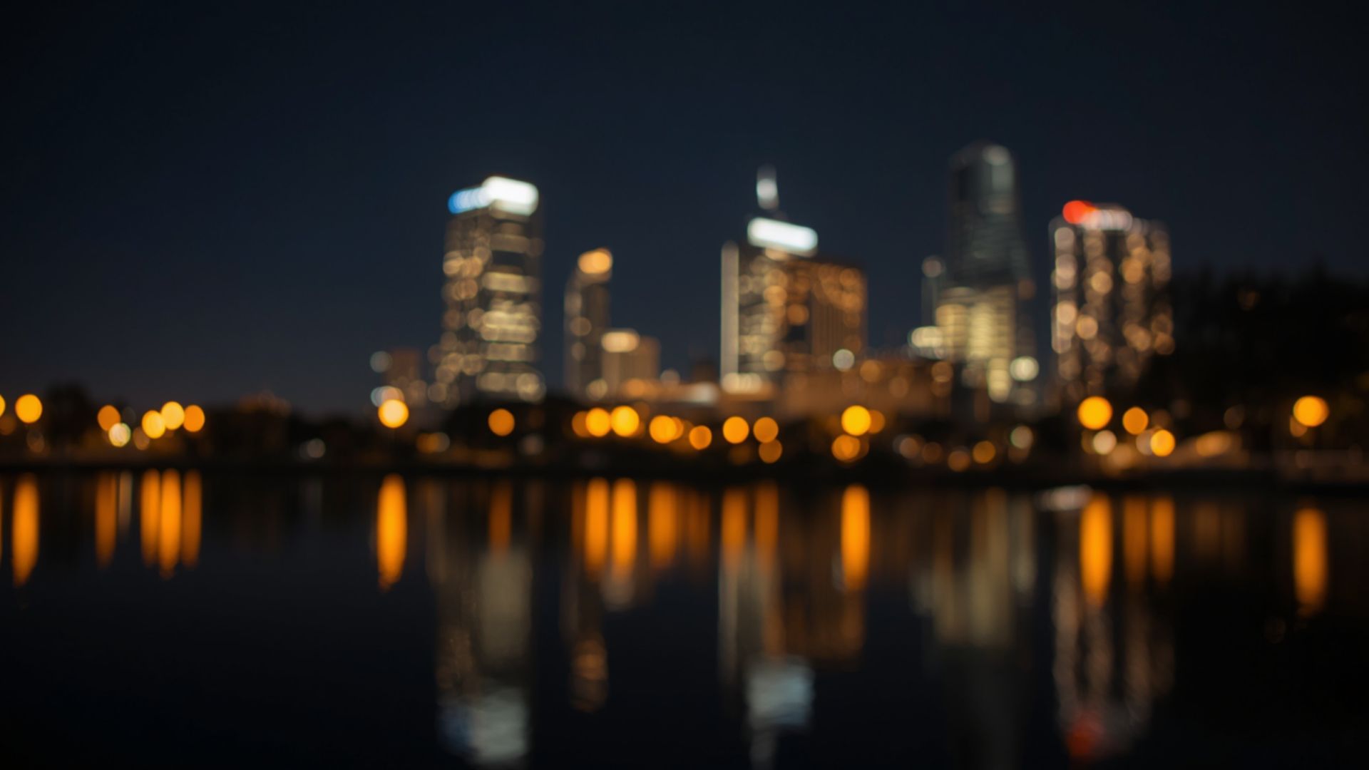 A blurred city skyline reflected on water at night.